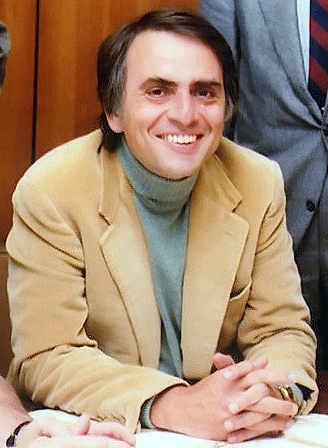 A man in a tan jacket sitting at a desk.