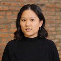 A woman in a black top standing in front of a brick wall.