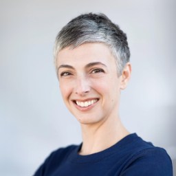 A woman with grey hair smiling in a blue shirt.