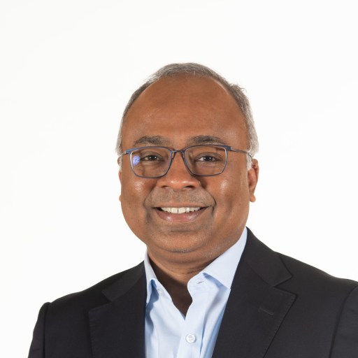 An indian man wearing glasses and a blue shirt.