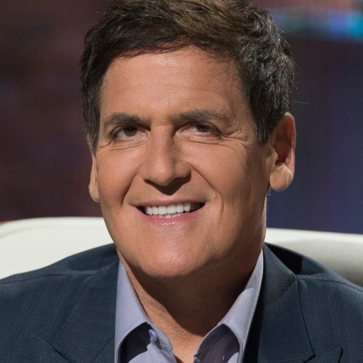 A smiling man in a suit sitting on a chair.