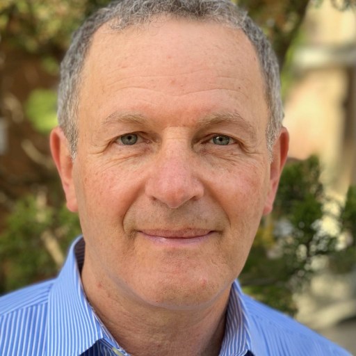 A man in a blue shirt standing in front of a tree.