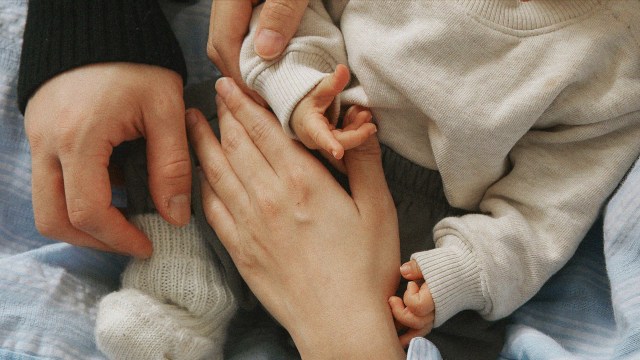A woman holding a baby's hand, symbolizing the bond between families.