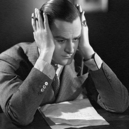 A man sitting at a desk in isolation, with his hands on his head.