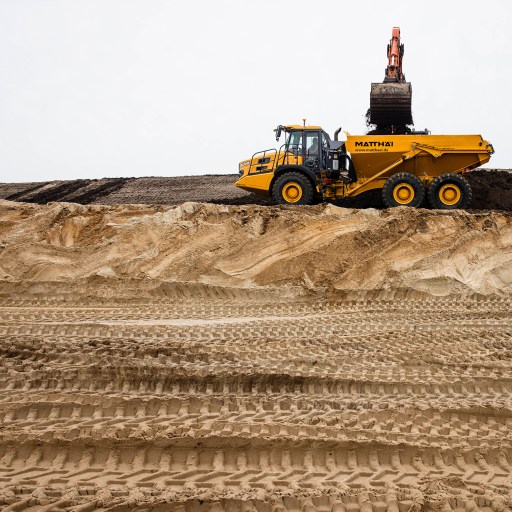 A yellow dump truck on a sand hill.