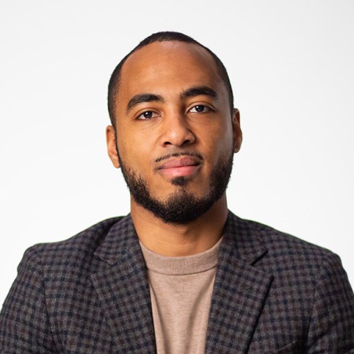 A black man in a blazer poses for a photo.