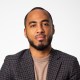A black man in a blazer poses for a photo.