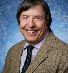 Professional portrait of a man in a suit and tie with a blue speckled background.
