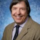 Professional portrait of a man in a suit and tie with a blue speckled background.