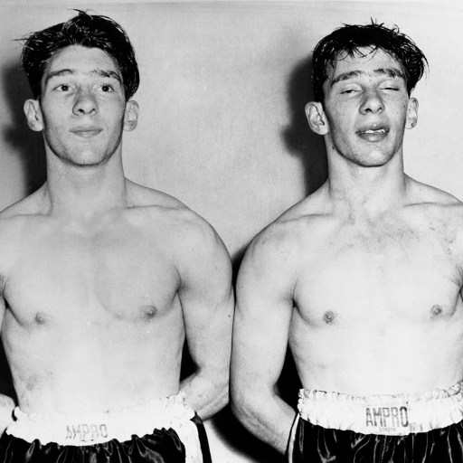 Two identical twin men in boxing gear standing next to each other.