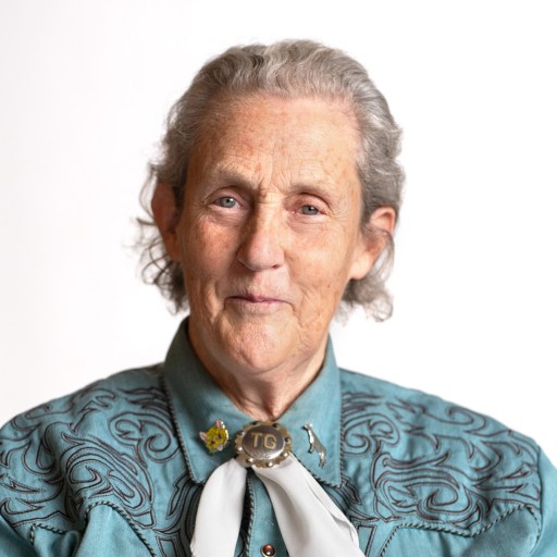 Elderly woman with a gentle smile wearing a turquoise blouse and a neck scarf.