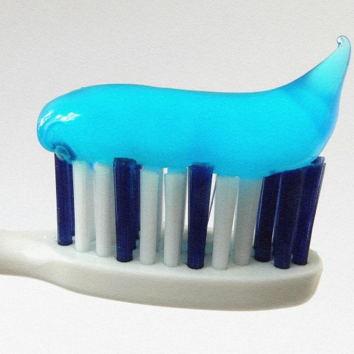 A toothbrush with blue and white bristles, topped with a large dollop of minty toothpaste.