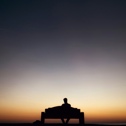 A person sitting on a bench silhouetted against a colorful sunset sky.
