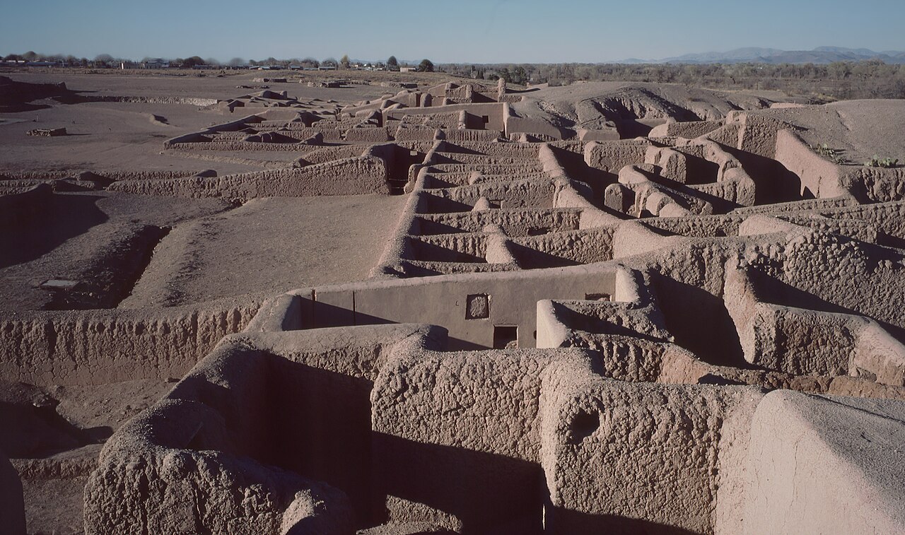 An aerial view of adobe ruins in Paquim&eacute;, Mexico, showcasing ancient walled structures and pathways under a clear sky with distant mountains.