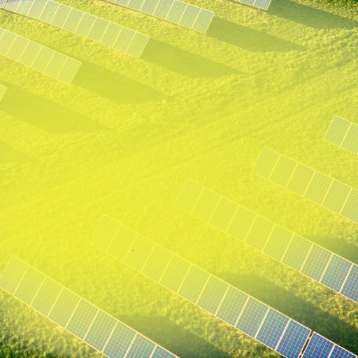 Aerial view of a solar farm with rows of solar panels installed on grassy fields on a sunny day.