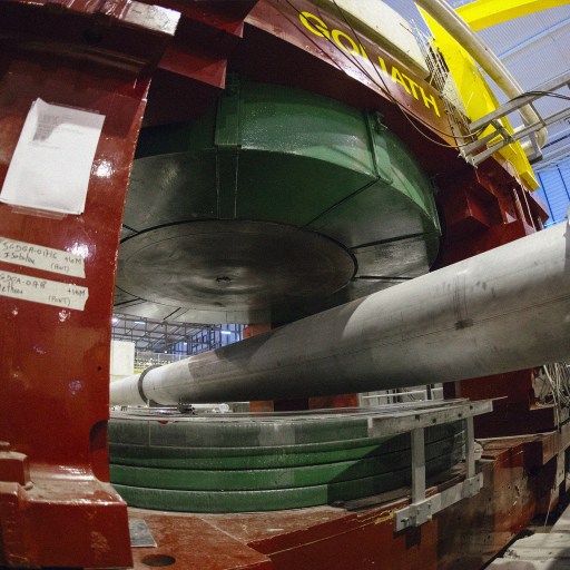 Image of a large industrial machine with a green cylindrical component and a long metal rod inside a red and gray structure.