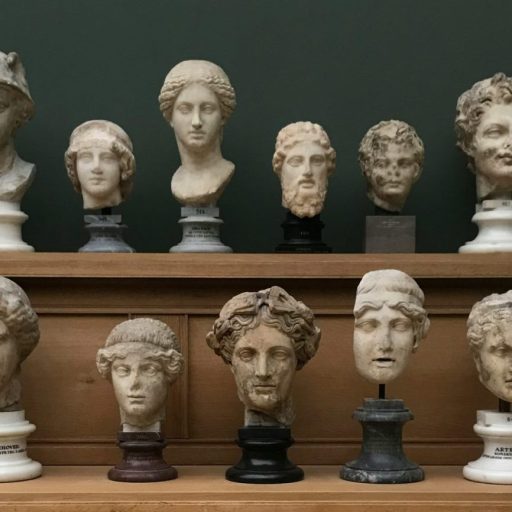 A display of various marble busts and sculptures arranged on two wooden shelves against a dark green wall.