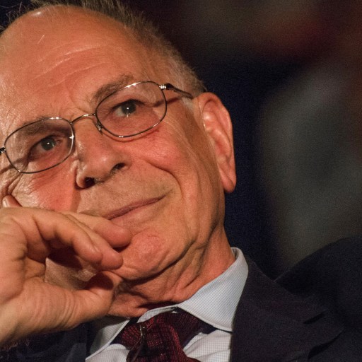 Kahneman wearing a suit, rests their chin on their hand while looking thoughtfully ahead.