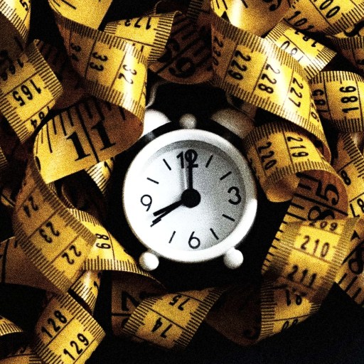 A small clock displaying 9:10 is surrounded by a tangled yellow measuring tape with black markings against a dark background, symbolizing the precision and commitment of intermittent fasting.