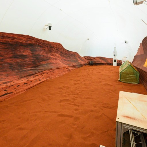 A room simulating a Martian landscape with red sand, rocky walls, a green tent, and NASA equipment.