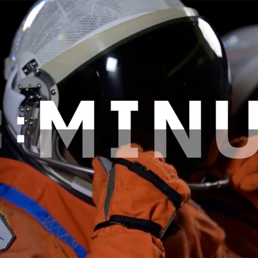 Two astronauts in orange spacesuits and helmets prepare for a mission. A digital countdown displays "T-MINUS," with an Artemis mission patch visible on one spacesuit.