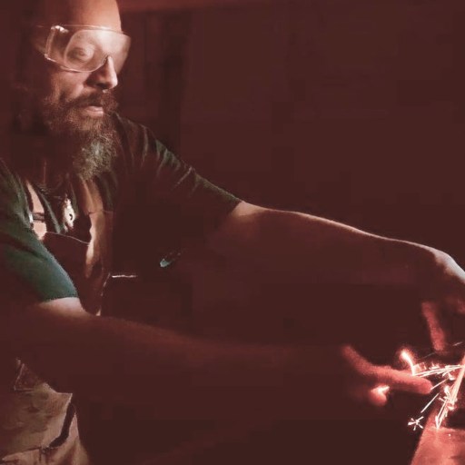 A person wearing safety goggles is using a tool to grind or cut metal, creating sparks in a dimly lit workshop.