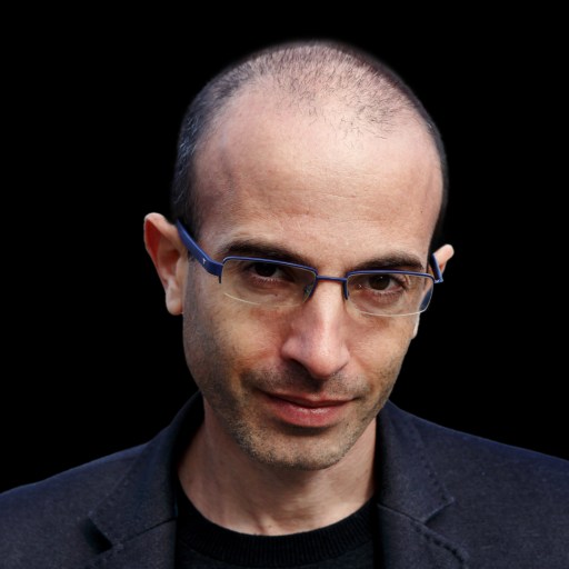 A person with glasses and a black blazer is looking directly at the camera against a black background.