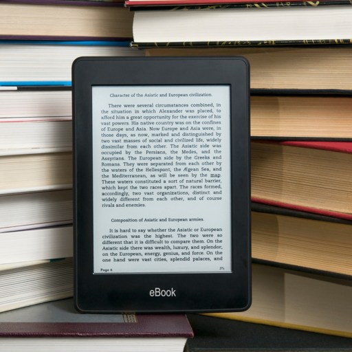 An e-reader displaying text is propped up against a stack of hardcover books.