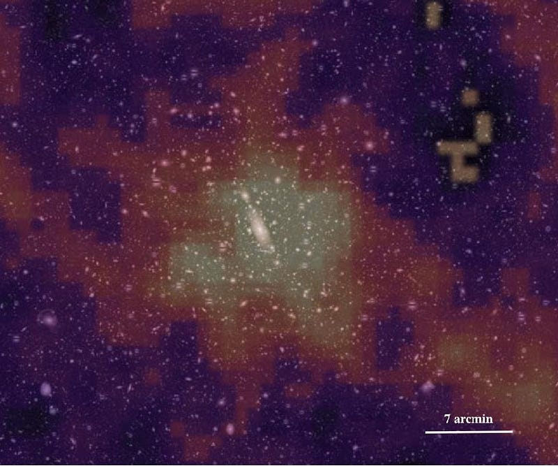 Grainy astronomical image showing a central elongated galaxy surrounded by colorful noise patterns. Scale indicator reads 7 arcmin.