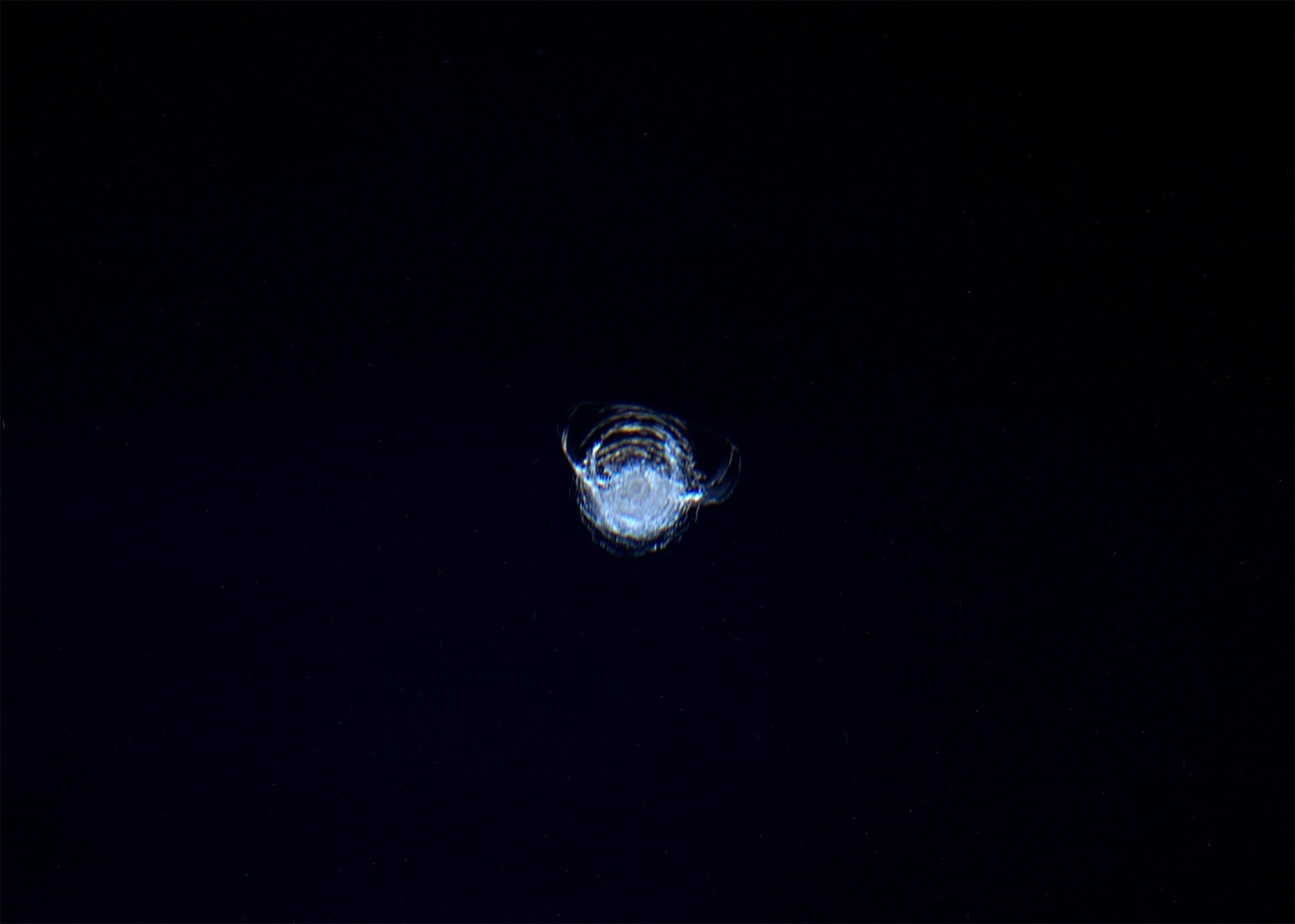 Close-up of a crack on a dark surface, showing a circular, spider-web pattern of fractured lines.