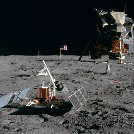 An astronaut stands proudly on the moon's surface near scientific equipment and a lunar lander, as the American flag waves in the background, symbolizing a pioneering USA nation.