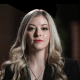 A woman with long blonde hair wearing a black suit and necklace.