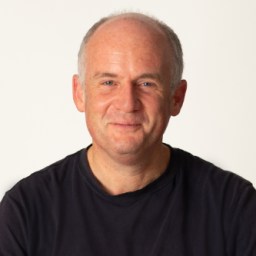 A person with a slight smile, wearing a black shirt, poses against a plain white background.