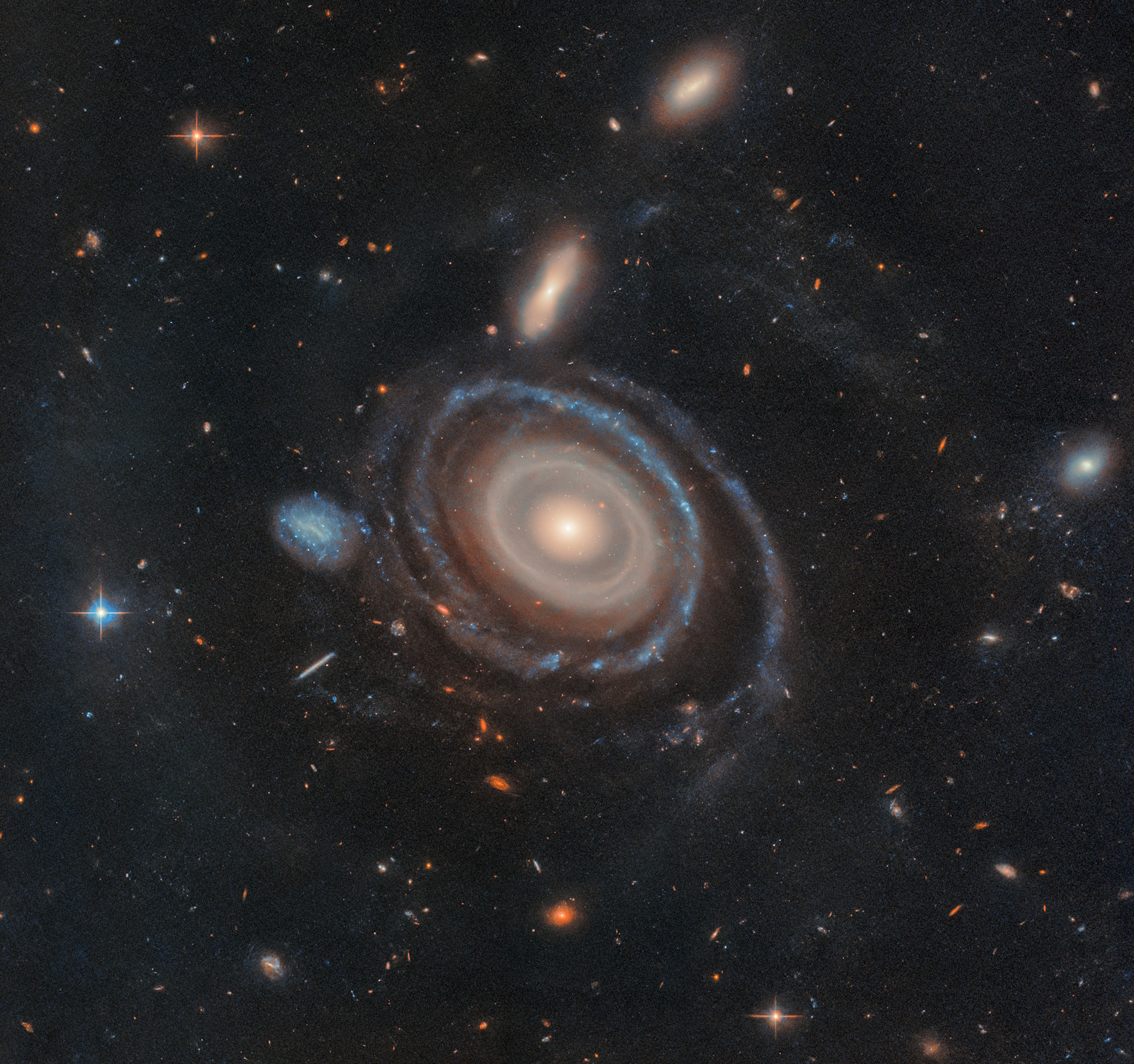 Image of a spiral galaxy with a bright core and distinct arms, resembling a bullseye ring galaxy. It is surrounded by various stars and smaller galaxies in space, creating an enchanting cosmic display.