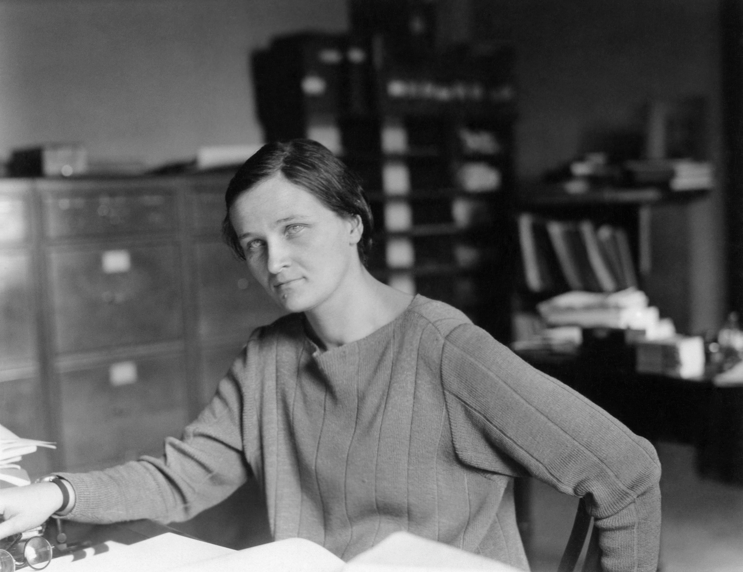 Amid an office setting brimming with files and papers, a person in a cozy sweater channels the curiosity of Cecilia Payne, diving deep into the mysteries at their desk.