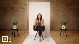 A person sitting on a chair in a studio setting with a white backdrop and two small tables on either side, each holding a small plant.