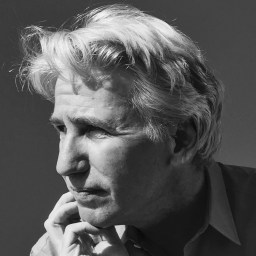 A black-and-white photo of a person with light hair, looking to the side, hand resting on the chin, with a contemplative expression.