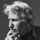 A black-and-white photo of a person with light hair, looking to the side, hand resting on the chin, with a contemplative expression.