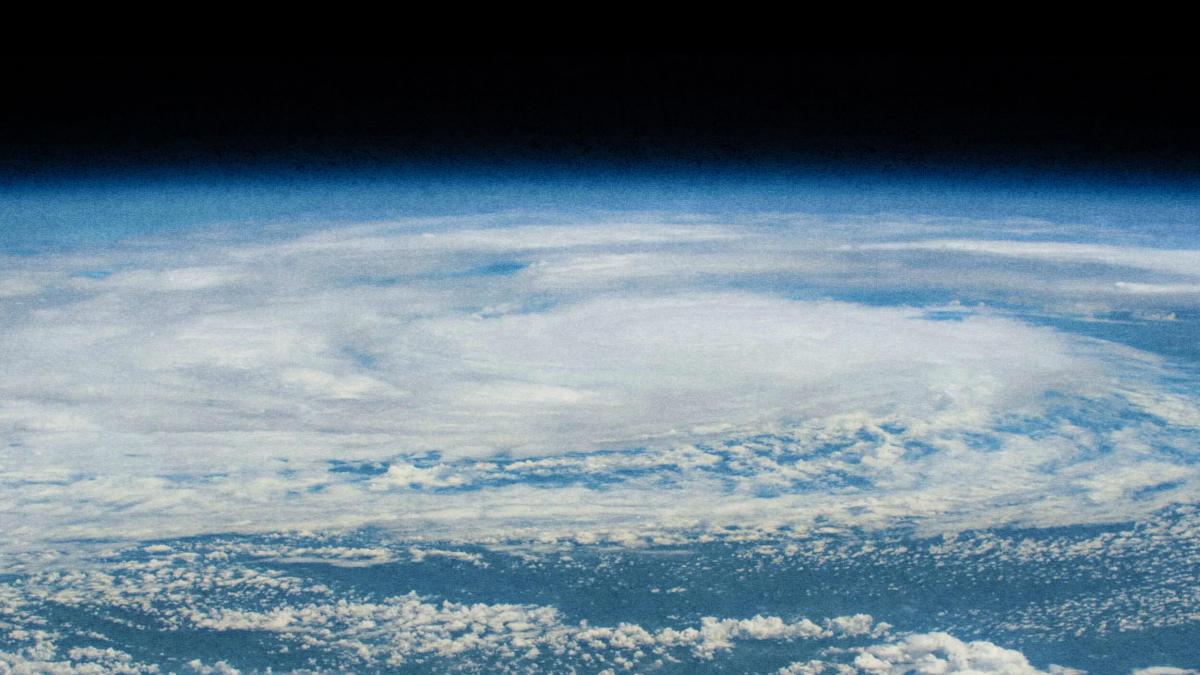 From a vantage point reminiscent of Carl Zimmer's explorations, an aerial view captures a massive swirling cloud formation over Earth, resembling a hurricane or cyclone against the infinite darkness of space.