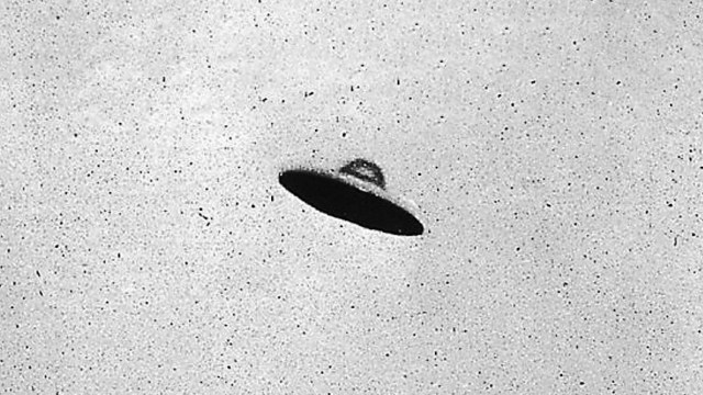 Black-and-white photo showing a disc-shaped object with a shadowed underside, floating in a blank sky—an iconic image from the UFO craze.