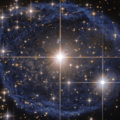 Bright star at the center of a blue nebula radiates mass energy, surrounded by numerous smaller stars, with diffraction spikes visible from the brightest stars.