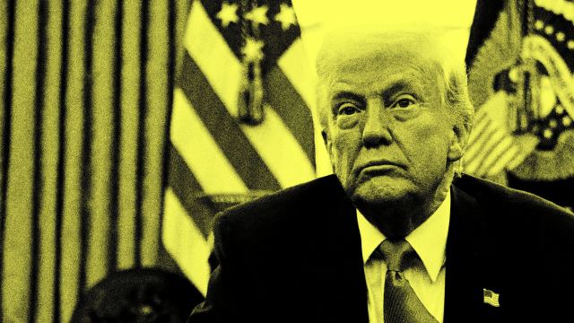 A man in a suit sits in front of American flags, his face partially shadowed and filtered in yellow tones.