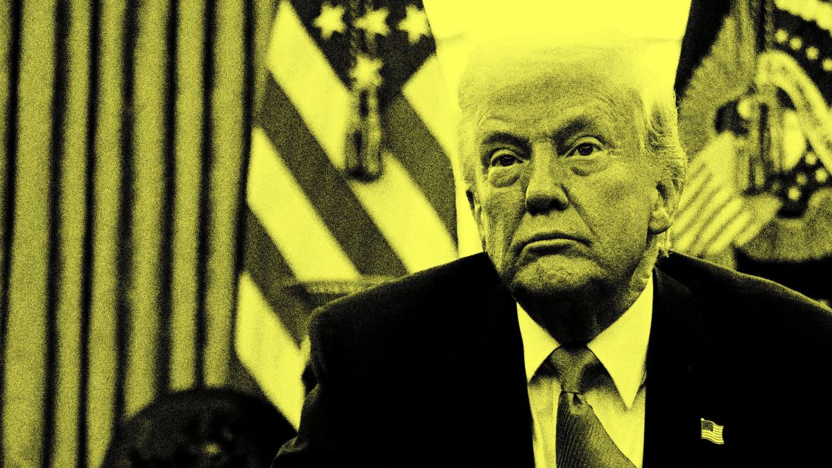 A man in a suit sits in front of American flags, his face partially shadowed and filtered in yellow tones.