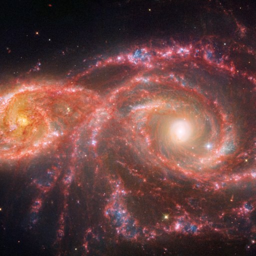 Two colorful spiral galaxies interacting in space, with bright centers and swirling arms of red, blue, and white hues, set against a backdrop of stars.