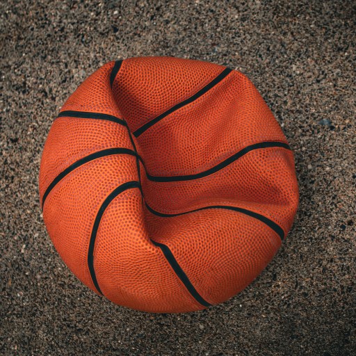 A deflated basketball lies on rough, textured ground.