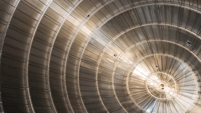 Close-up of a large, metallic, circular structure with concentric rings and radial lines, illuminated by natural light from one side—evoking experiments that revealed the neutrino mass is smaller than once believed.