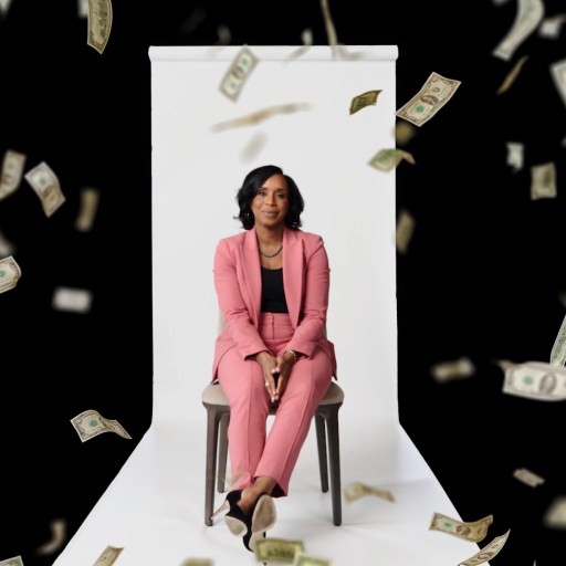A woman in a pink suit sits on a chair against a white backdrop while U.S. dollar bills fall around her on a black background.