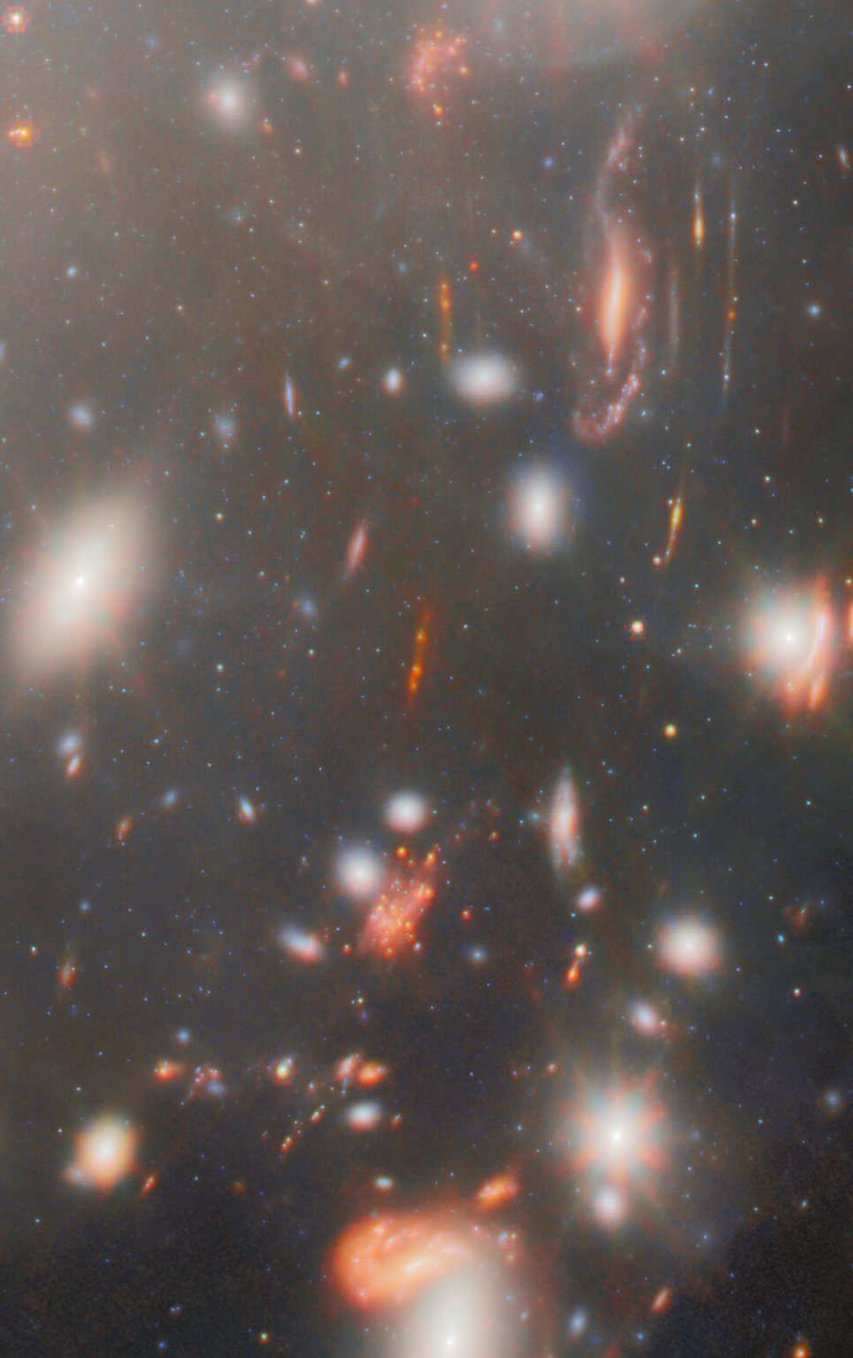 A field of distant galaxies in deep space, captured by JWST, shows various shapes and colors—some blurred and stretched by the universe’s most extreme gravitational lens.