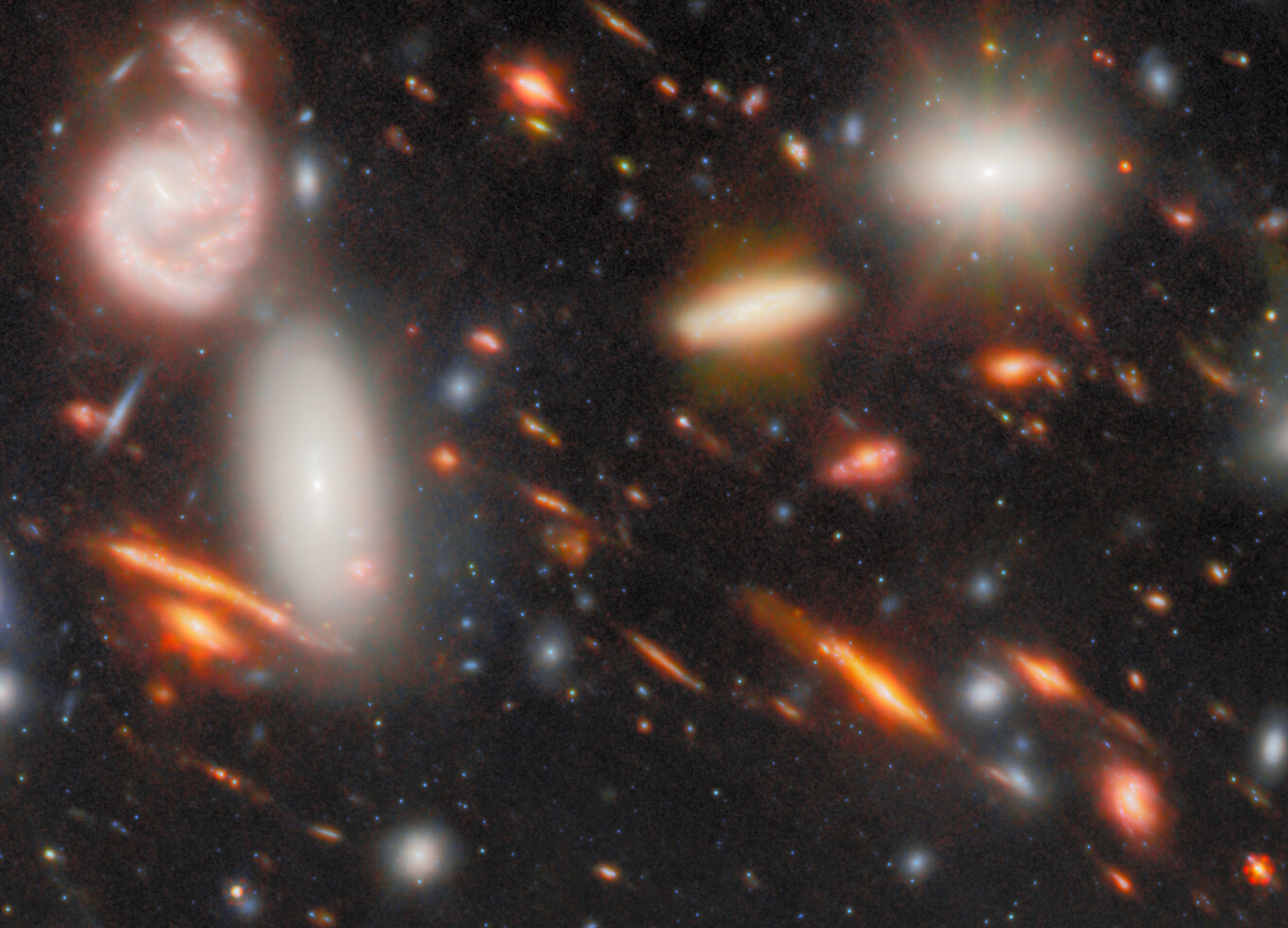 A deep space image from JWST shows numerous galaxies of varying shapes and colors, with bright, glowing stars and hazy, elongated light patterns—evidence of the most extreme gravitational lens—against a dark background speckled with small stars.