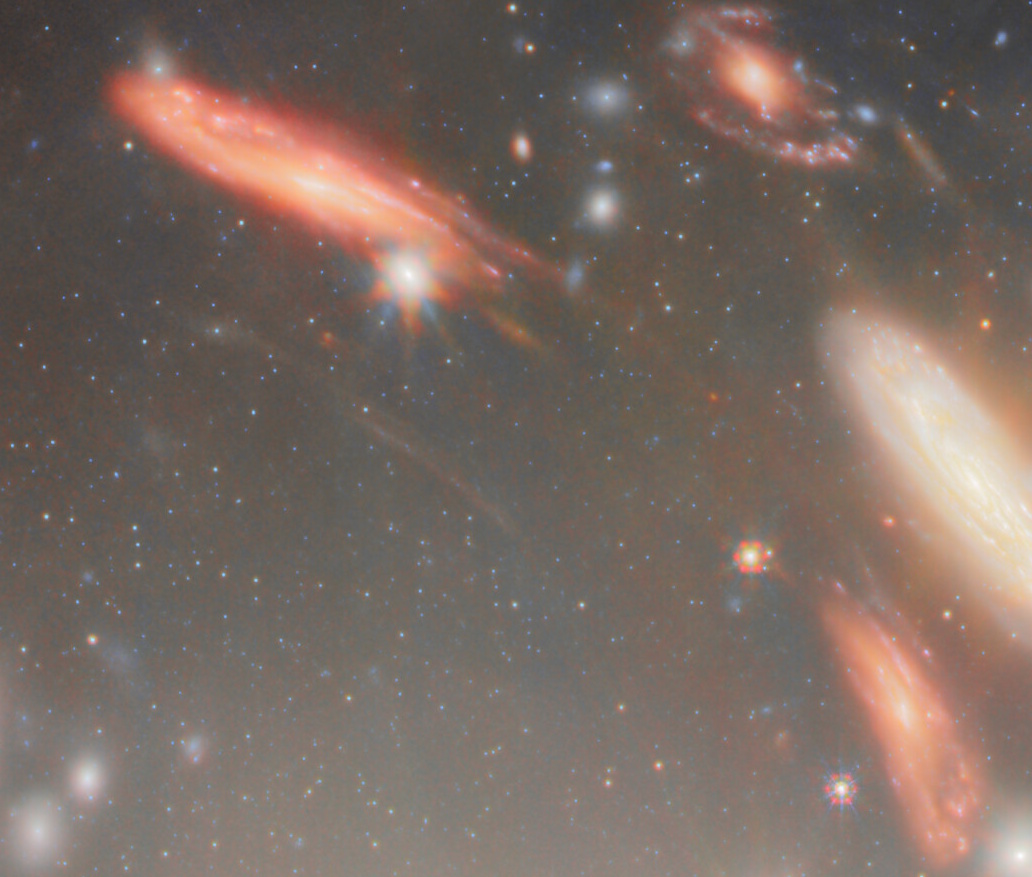 Image of several bright, colorful galaxies and numerous stars scattered across a dark space background, captured through the JWST’s most extreme gravitational lens.